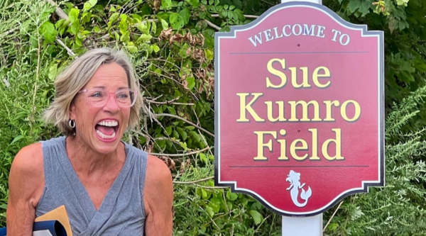 Sue Kumro smiles next to the sign for the park named in her honor