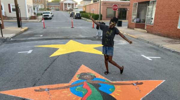 A young artist poses behind her Juneteenth street mural