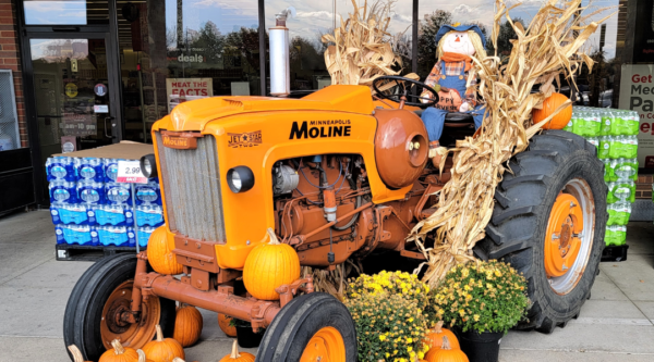 Small orange tractor decorated with pumpkins, hay, and a scarecrow