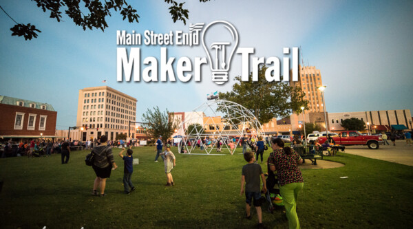 Green lawn with half-circle sculpture with people walking on lawn, with text over image reading, "Main Street End Maker Trail"